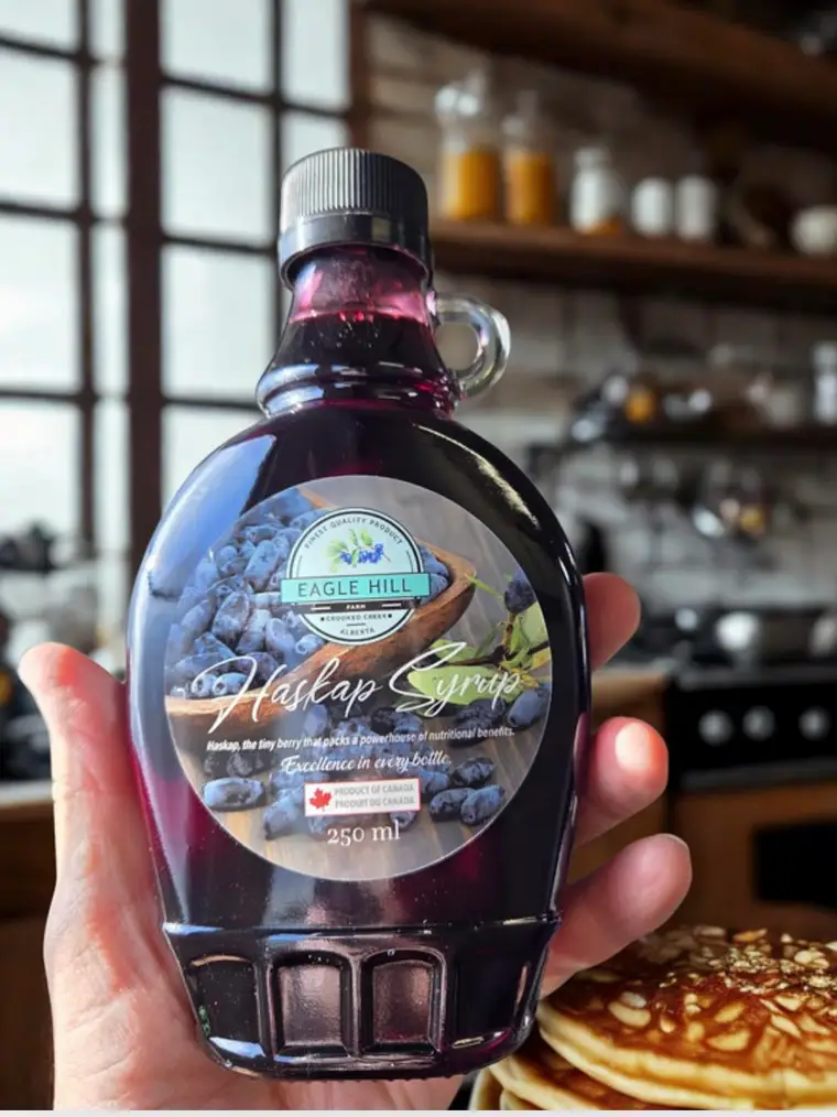 A bottle of Eagle Hill Farm haskap syrup held over a stack of pancakes