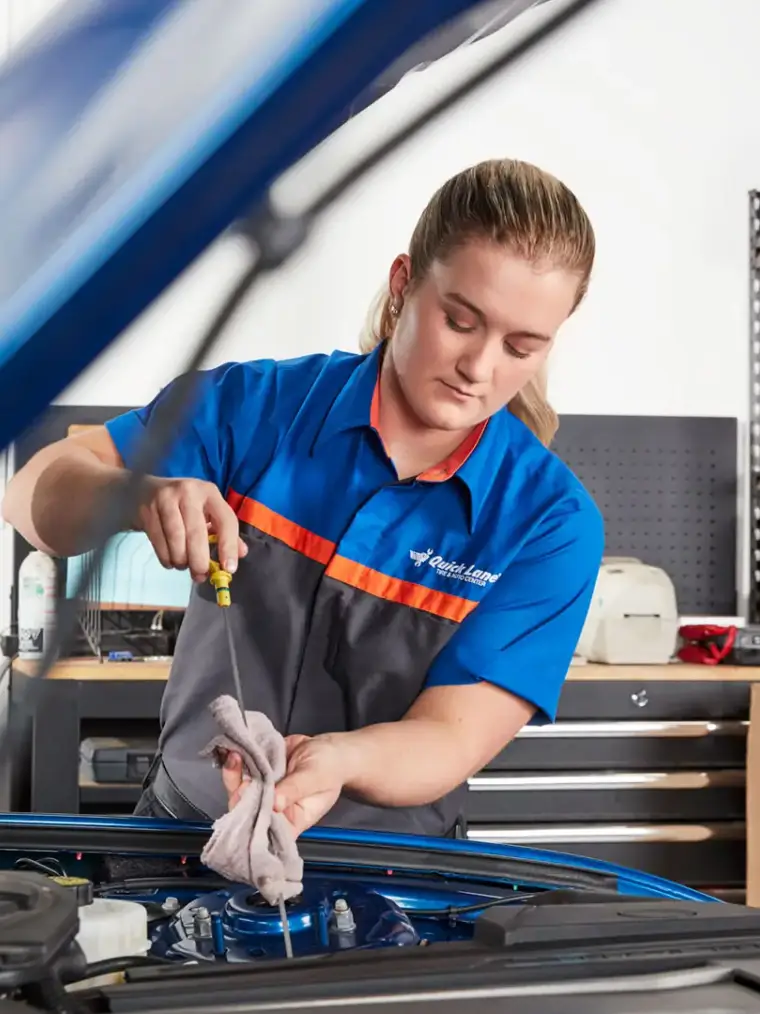 A Quick Lane technician working under the hood of a vehicle in the service bay