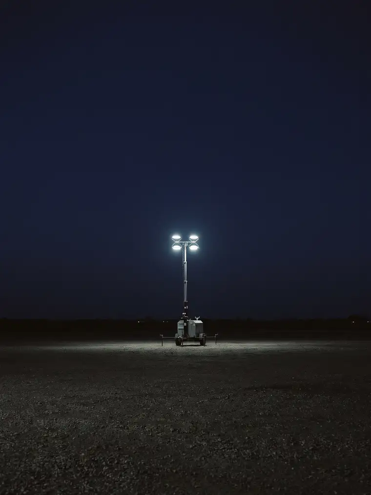 A portable light tower raised against a night sky on a gravel lease site