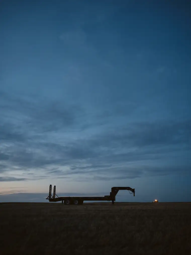 An equipment trailer silhouetted on a flat prairie horizon at blue hour