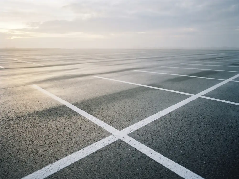 An empty asphalt lot at dawn with painted parking lines converging
